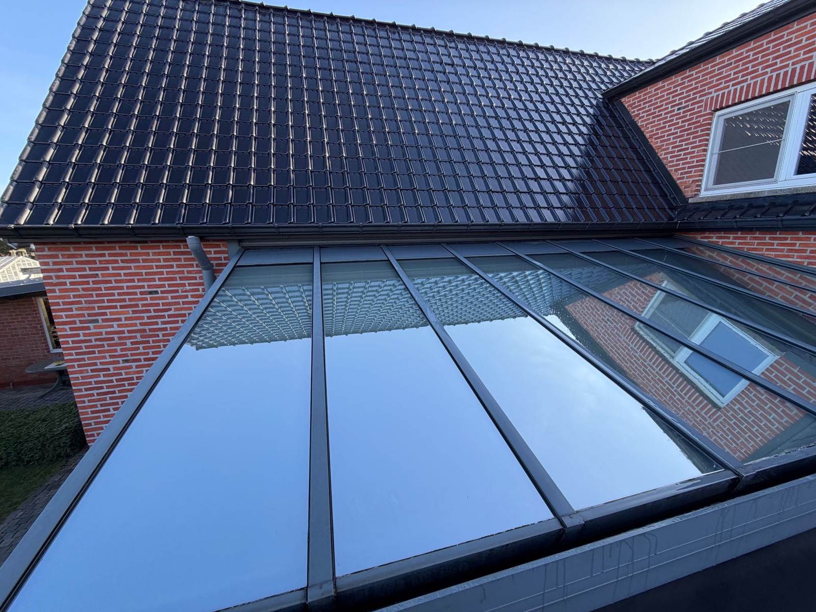 Glazen dakconstructie met zwarte dakpannen door Dakwerken Martens